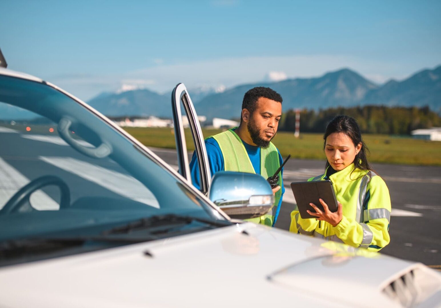 Airfield operations officers monitoring and maintaining flight records. Wearing reflective clothes using a digital tablet and a walkie talkie to communicate with air traffic control.